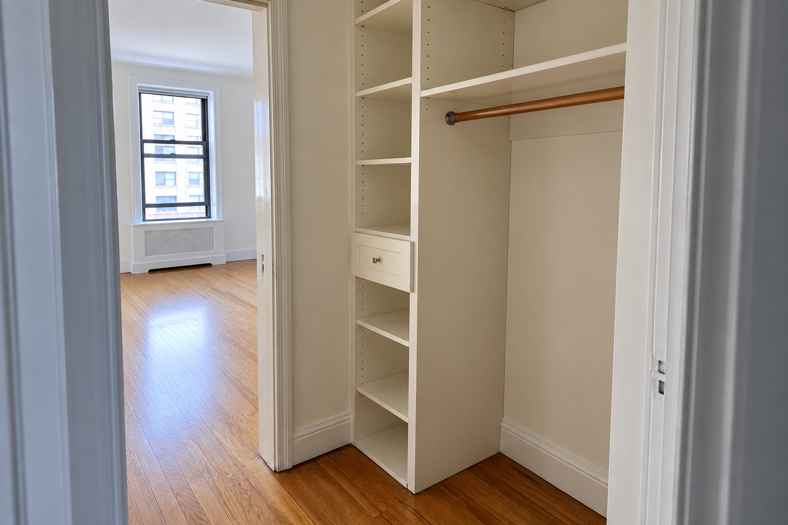 Generic empty built-in closet with shelves, drawer and hanging rod beside an unfurnished room